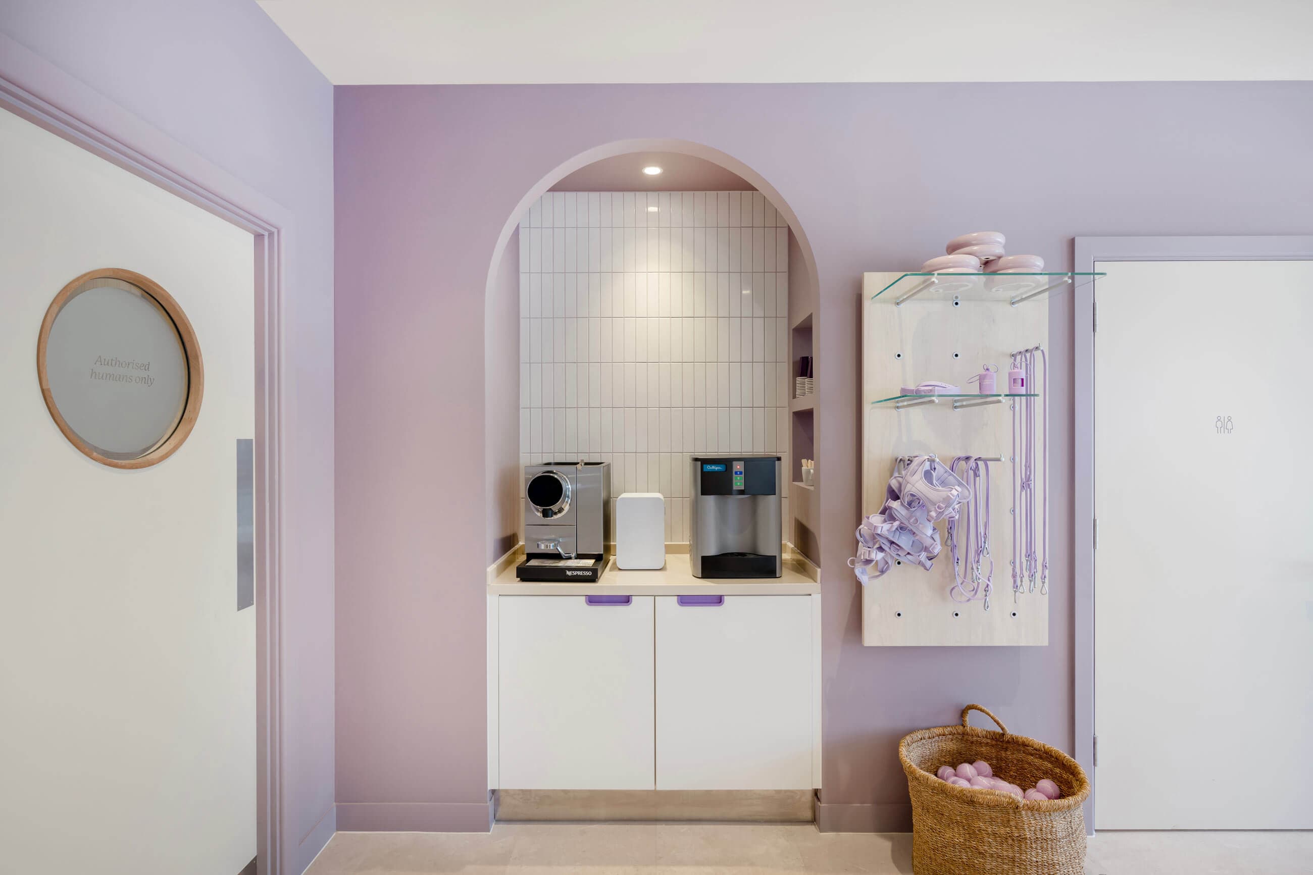 A modern service area with a purple theme, featuring coffee machines, accessories on shelves, and a basket of pastel decor.