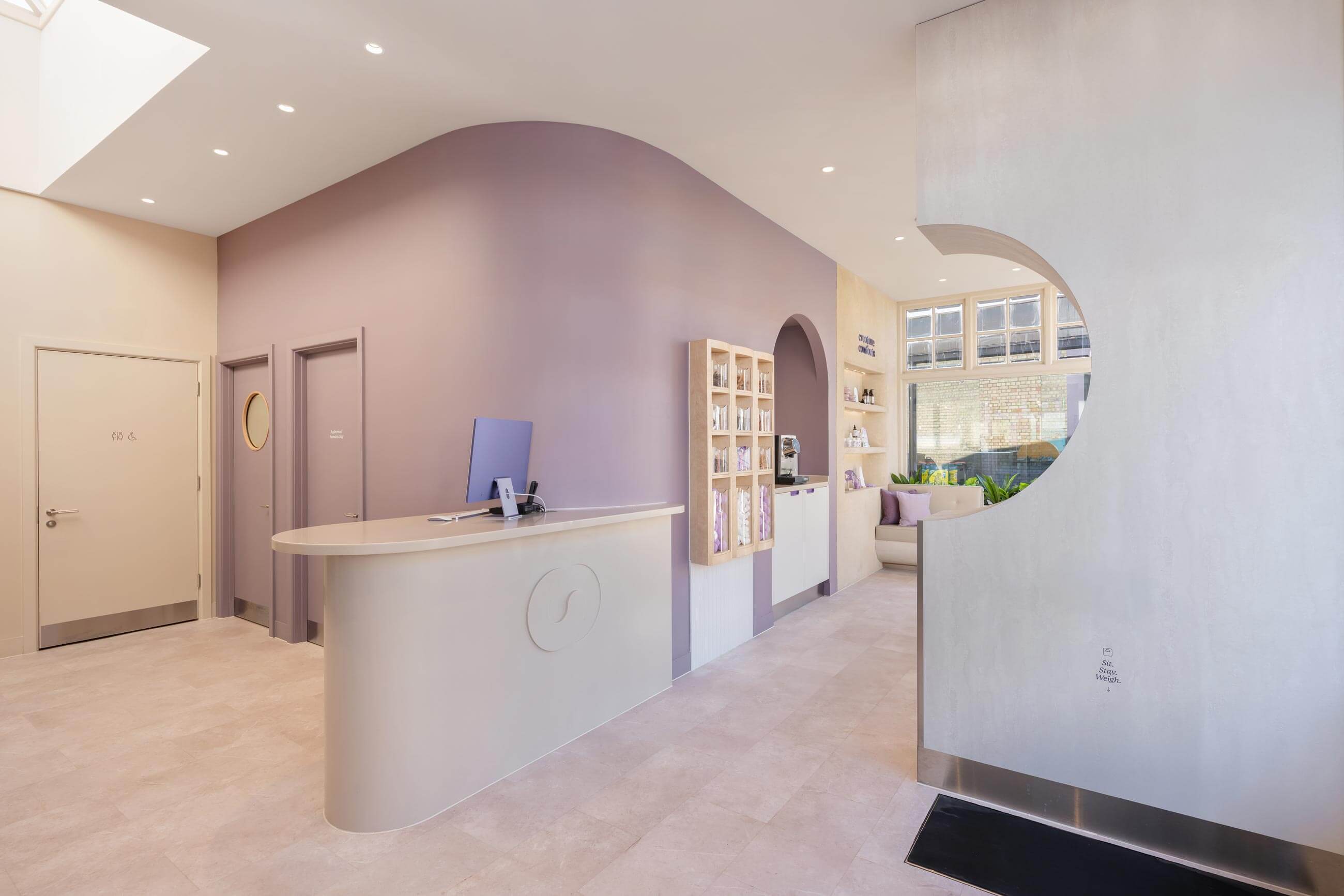 Modern reception area with soft lighting, curved walls, a front desk, and stylish decor, creating a welcoming atmosphere.